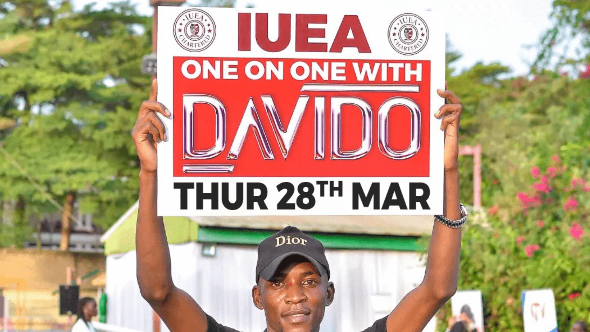 With excitement, IUEA staff member Ssali Gerald shares details about Davido’s exclusive press conference at IUEA, slated for March 28, 2024, through a vibrant placard display.